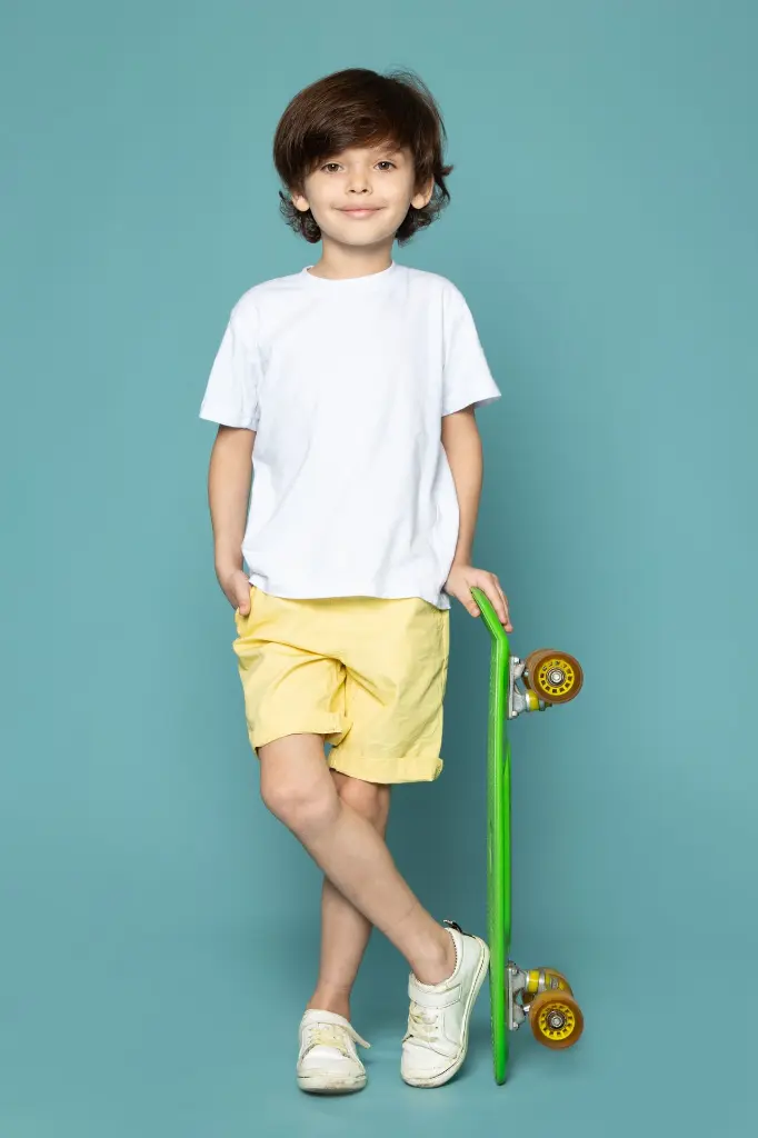 une-vue-de-face-mignon-enfant-garcon-en-t-shirt-blanc-et-jean-jaune-tenant-une-planche-a-roulettes-verte-sur-le-sol-bleu.webp